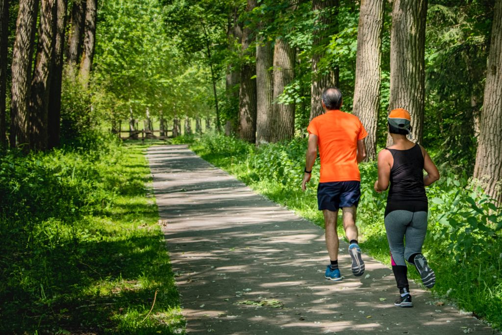 LongevityLifeextensionthroughnaturalscientificmethods Two people, a man and a woman, jogging on a lush green forest trail, enjoying exercise and the tranquility of nature for a healthy lifestyle.
