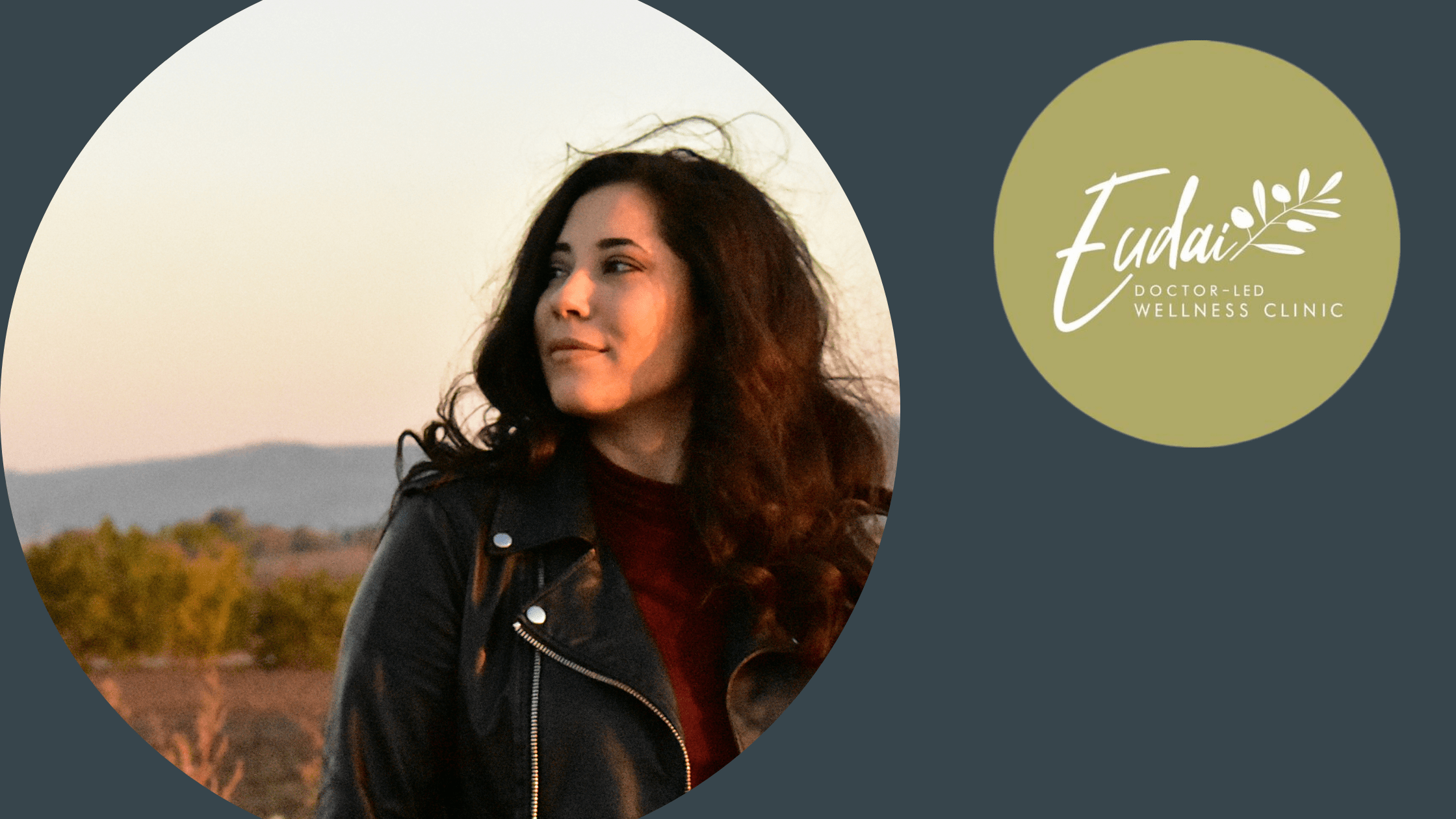 A woman with long dark hair stands outdoors in the golden light of sunset. She is wearing a black leather jacket, gazing off to the side with a calm expression. The landscape behind her is slightly blurred, featuring trees and hills.